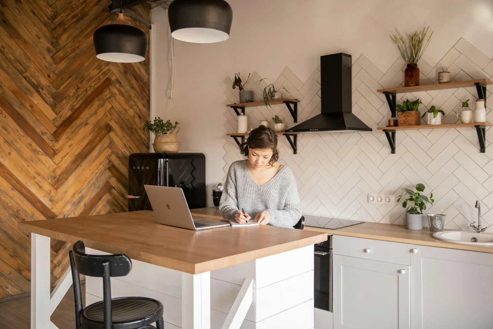 Nữ doanh nhân trẻ mặc áo xám ngồi làm việc tại quầy bếp với laptop và sổ tay trong không gian gia đình tiện nghi. | Thiết kế nội thất 24