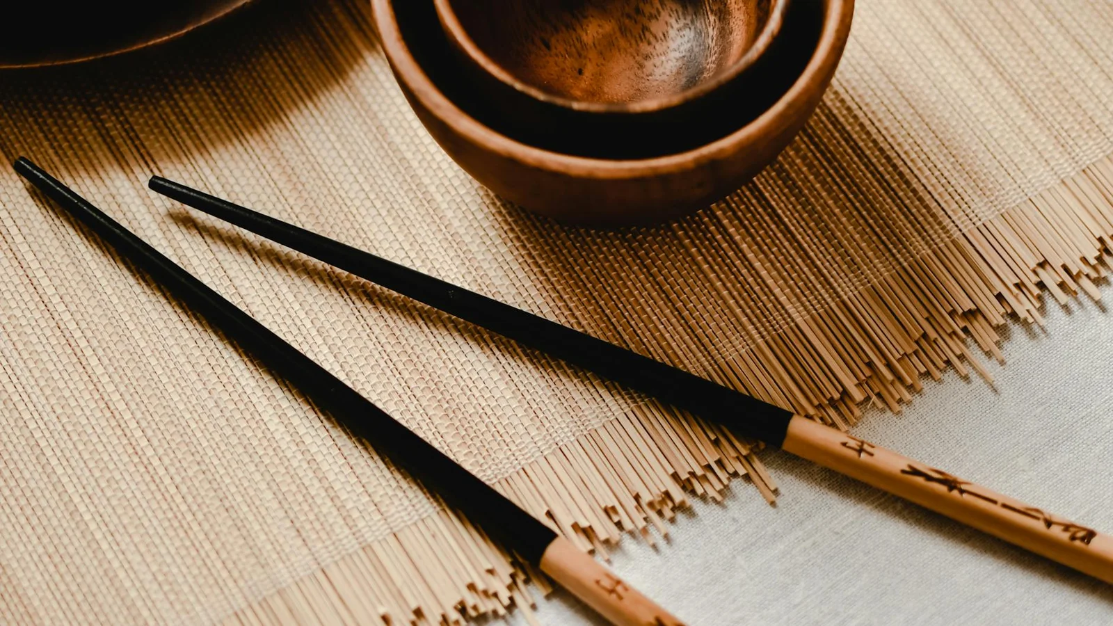 Bộ đồ ăn mộc mạc gồm bát gỗ và đũa tre đặt trên thảm cói thể hiện nét đẹp ẩm thực Á thuần khiết. | Thiết kế nội thất 24