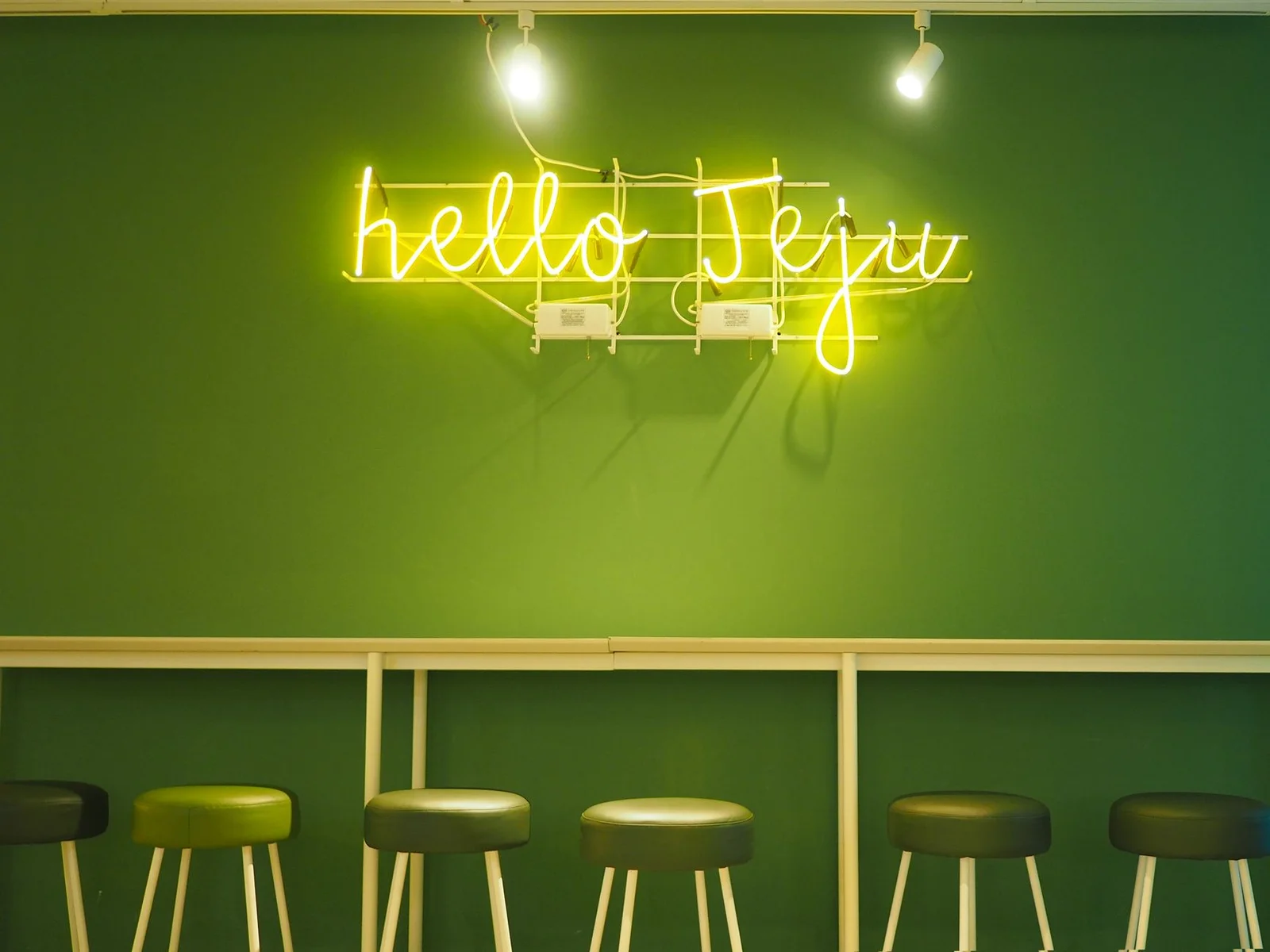 Góc không gian trẻ trung nổi bật với biển hiệu đèn neon chữ Hello Jeju cùng dãy ghế xanh lá hài hòa với tường nền. | Thiết kế nội thất 24
