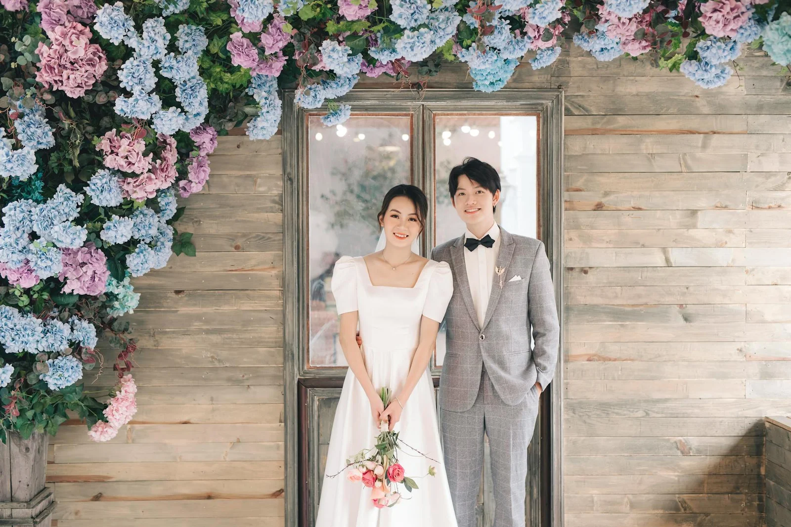 Cặp đôi tân hôn rạng rỡ chụp hình trước phông nền hoa lá rực rỡ, gợi ý trang trí đám cưới phong cách Hàn Quốc. | Thiết kế nội thất 24
