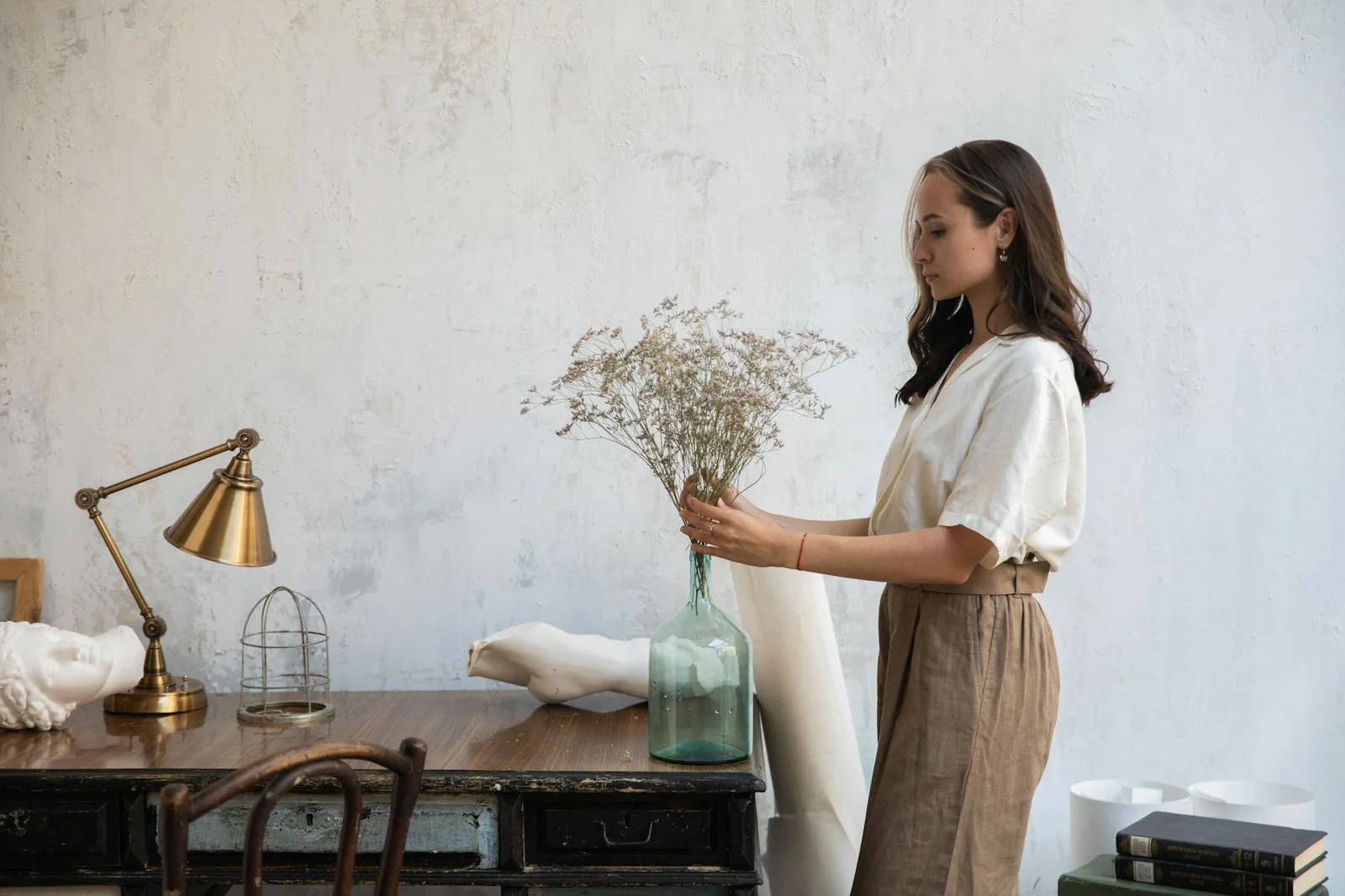Người phụ nữ khéo léo cắm hoa giữa không gian làm việc trong nhà mang phong cách cổ điển cùng bàn và đèn đọc sách. | Thiết kế nội thất 24
