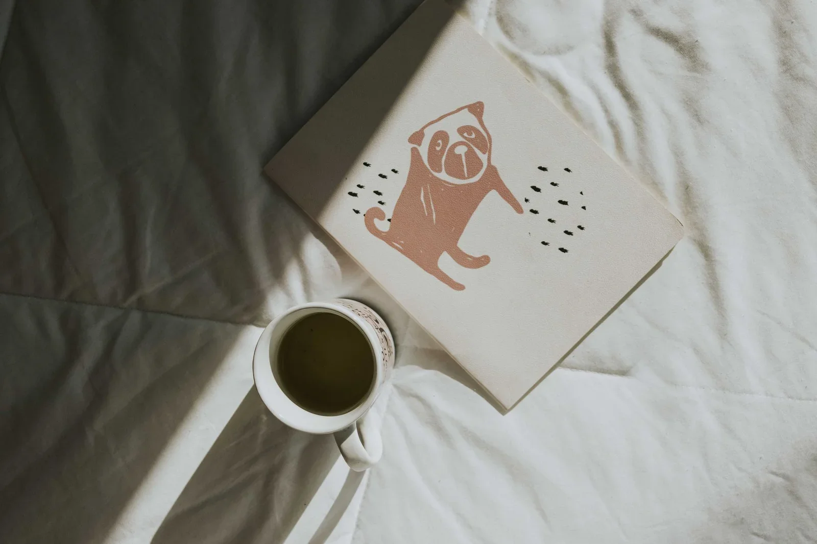 Góc giường ngập nắng sớm với tách cà phê thơm và cuốn sách minh họa dễ thương, khơi gợi cảm hứng sống chậm thư giãn. | Thiết kế nội thất 24
