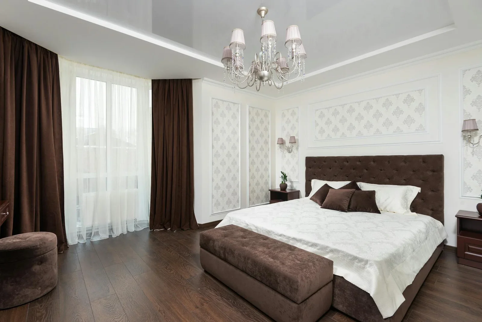 Phòng ngủ đương đại với đèn chùm sang trọng, sắc nâu trầm ấm và giường nệm êm ái, cân bằng lý tưởng cho góc làm việc. | Thiết kế nội thất 24