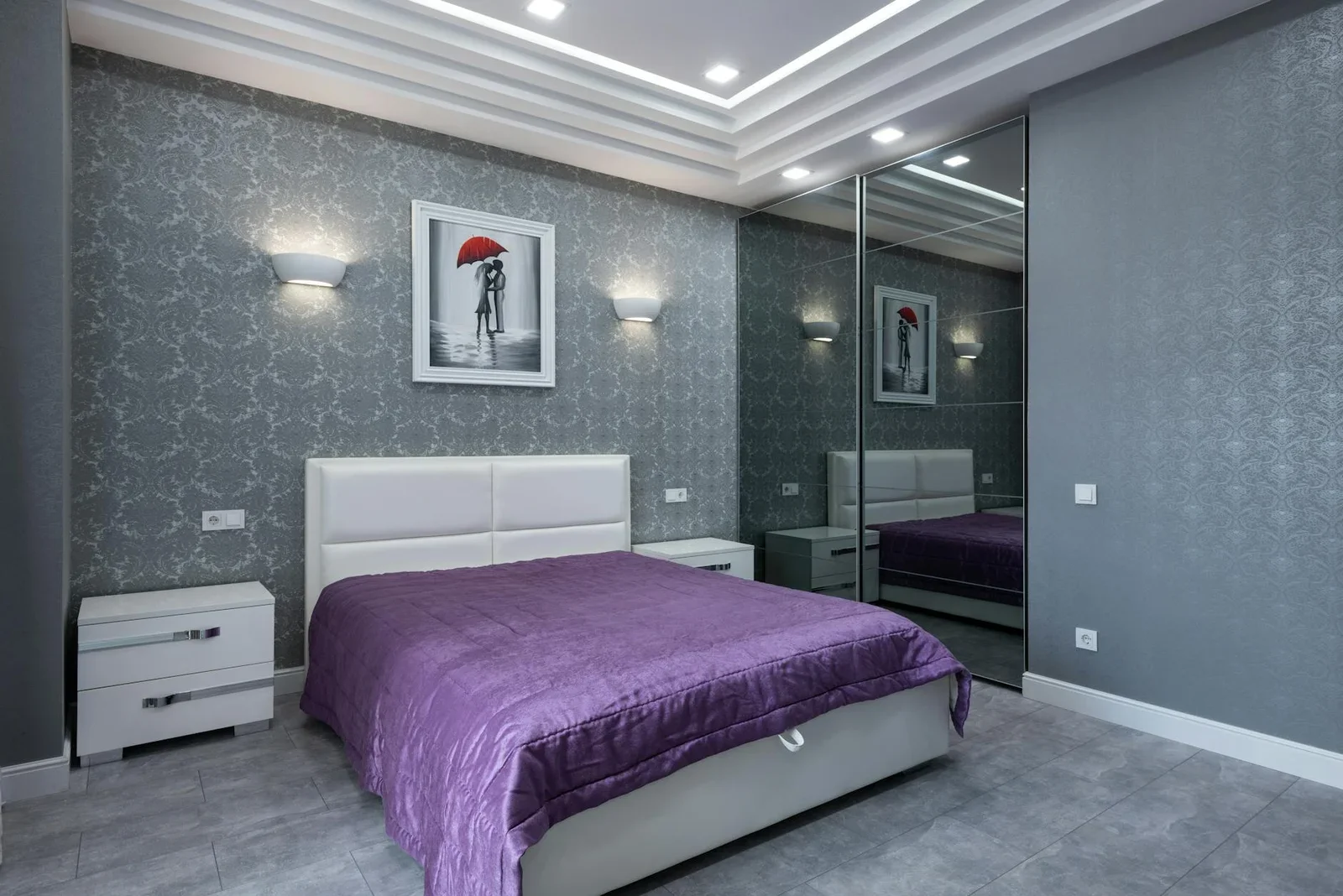 Phòng ngủ hiện đại với tường xám trang nhã, giường chăn tím nổi bật cùng tủ cánh kính và nội thất tông sáng hài hòa. | Thiết kế nội thất 24