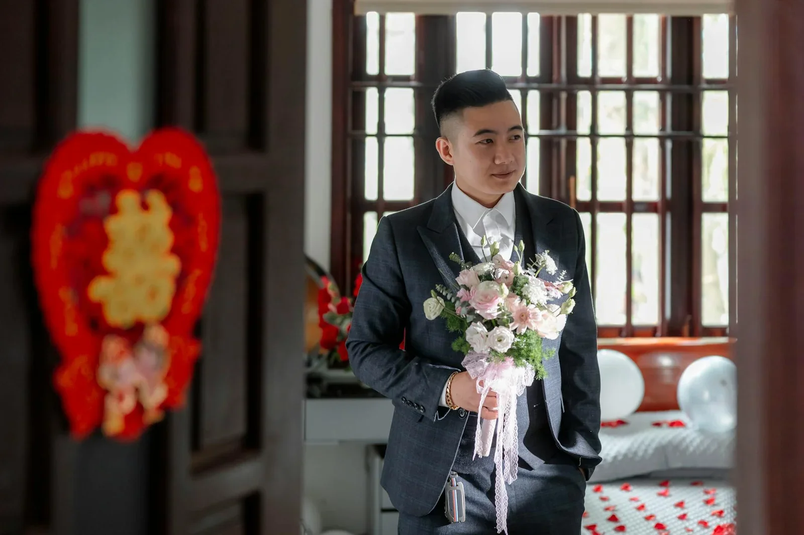 Chú rể lịch lãm cầm hoa đứng giữa phòng ngủ lãng mạn, nơi nội thất trang nhã tôn lên vẻ đẹp Indochine đậm chất thơ. | Thiết kế nội thất 24