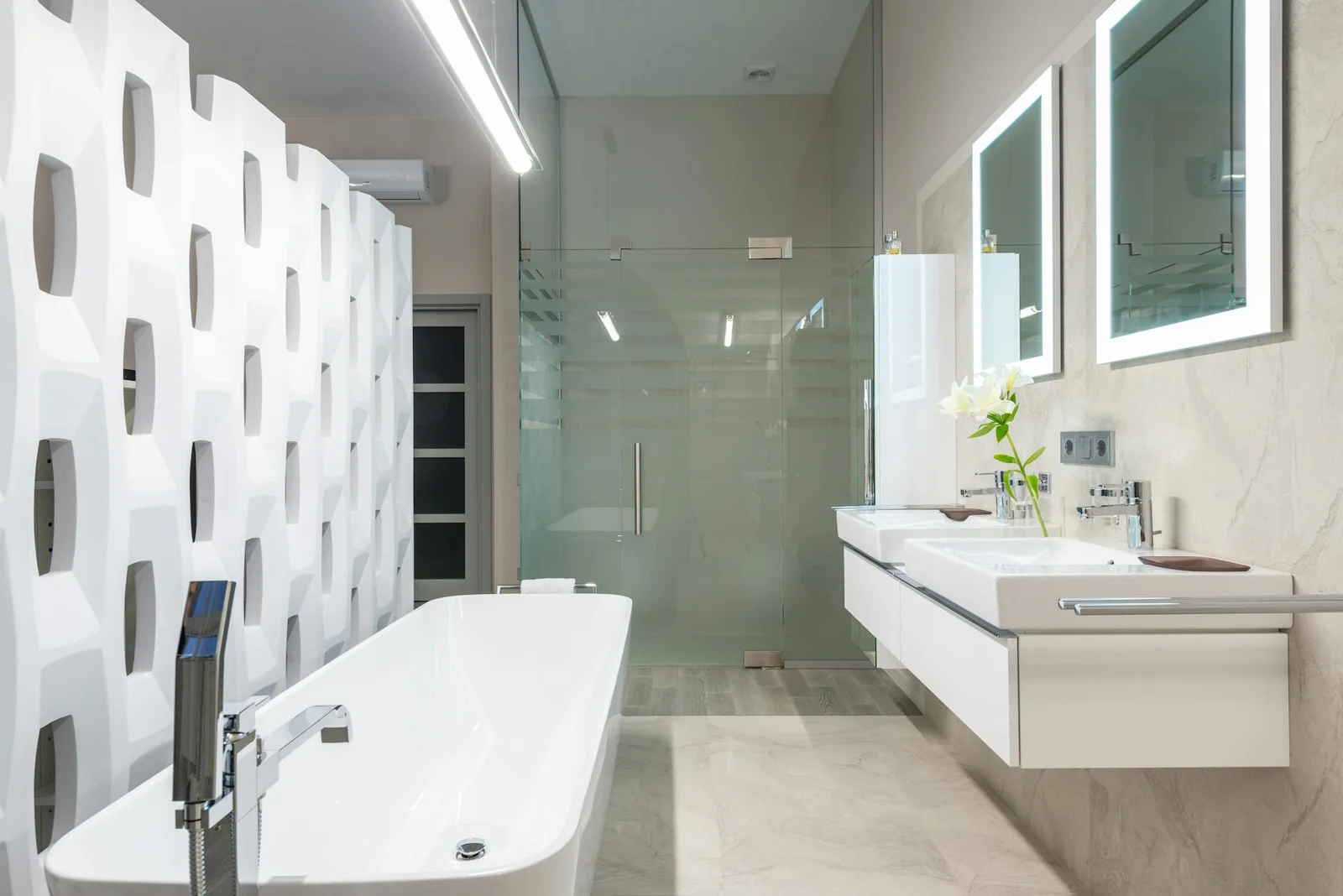 Bồn tắm trắng tinh khôi đặt cạnh vách ngăn trang trí, gần chậu rửa, gương soi và buồng tắm kính trong phòng tắm sáng sủa. | Thiết kế nội thất 24