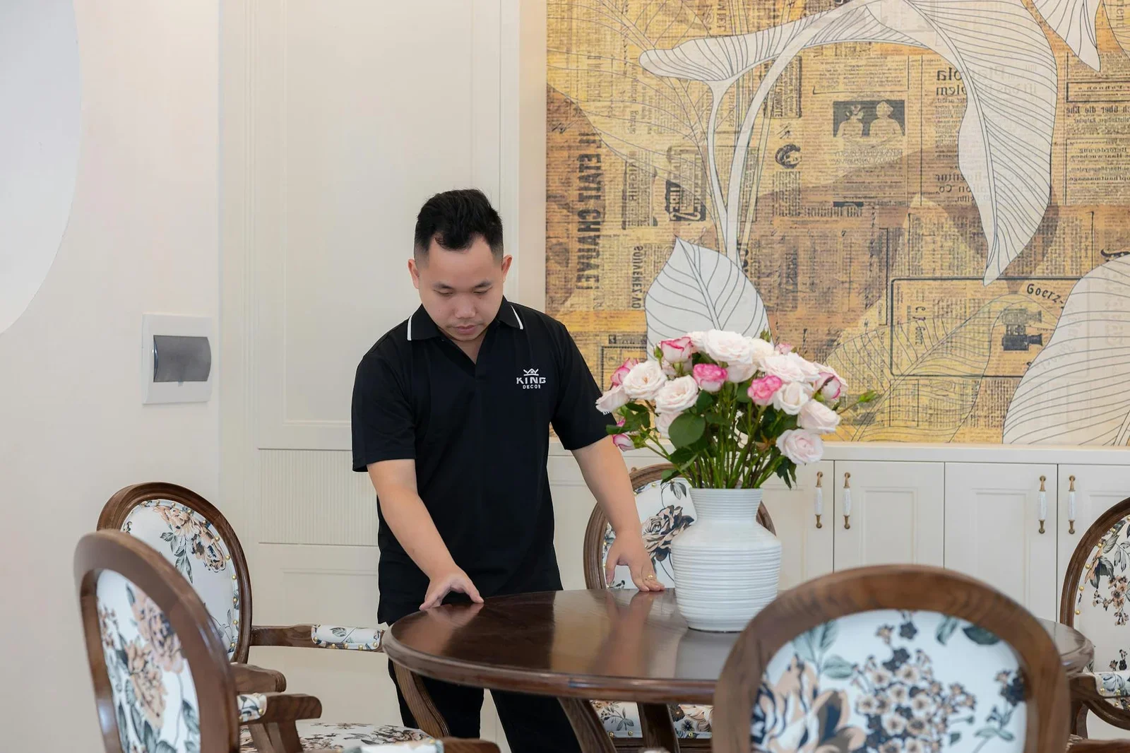 A man arranging flowers on a wooden table indoors, creating  | Thiết kế nội thất 24