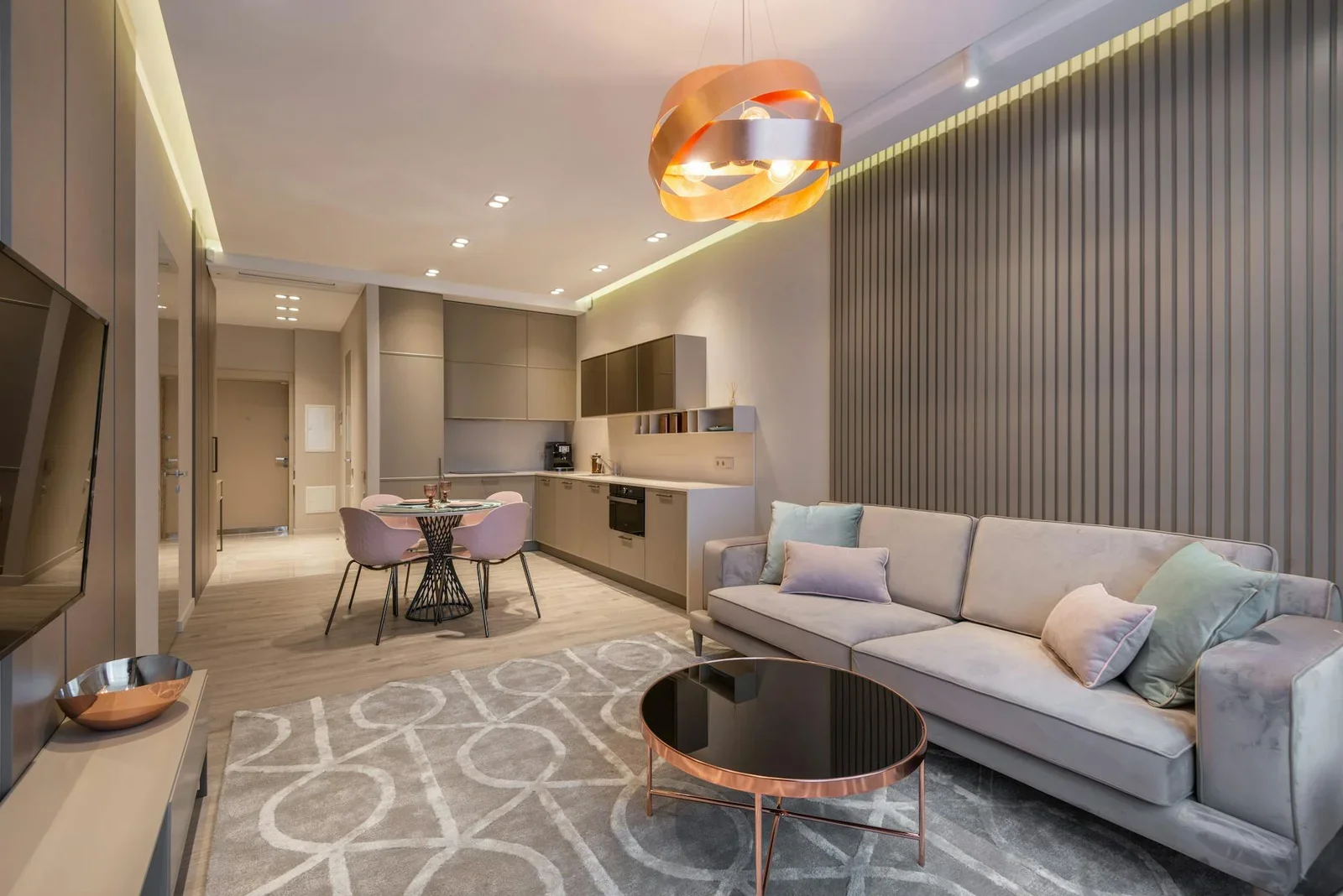 Ghế sofa êm ái đặt cạnh bàn trà tròn gần khu bếp, nổi bật dưới ánh sáng đèn chùm nghệ thuật đầy cảm hứng. | Thiết kế nội thất 24
