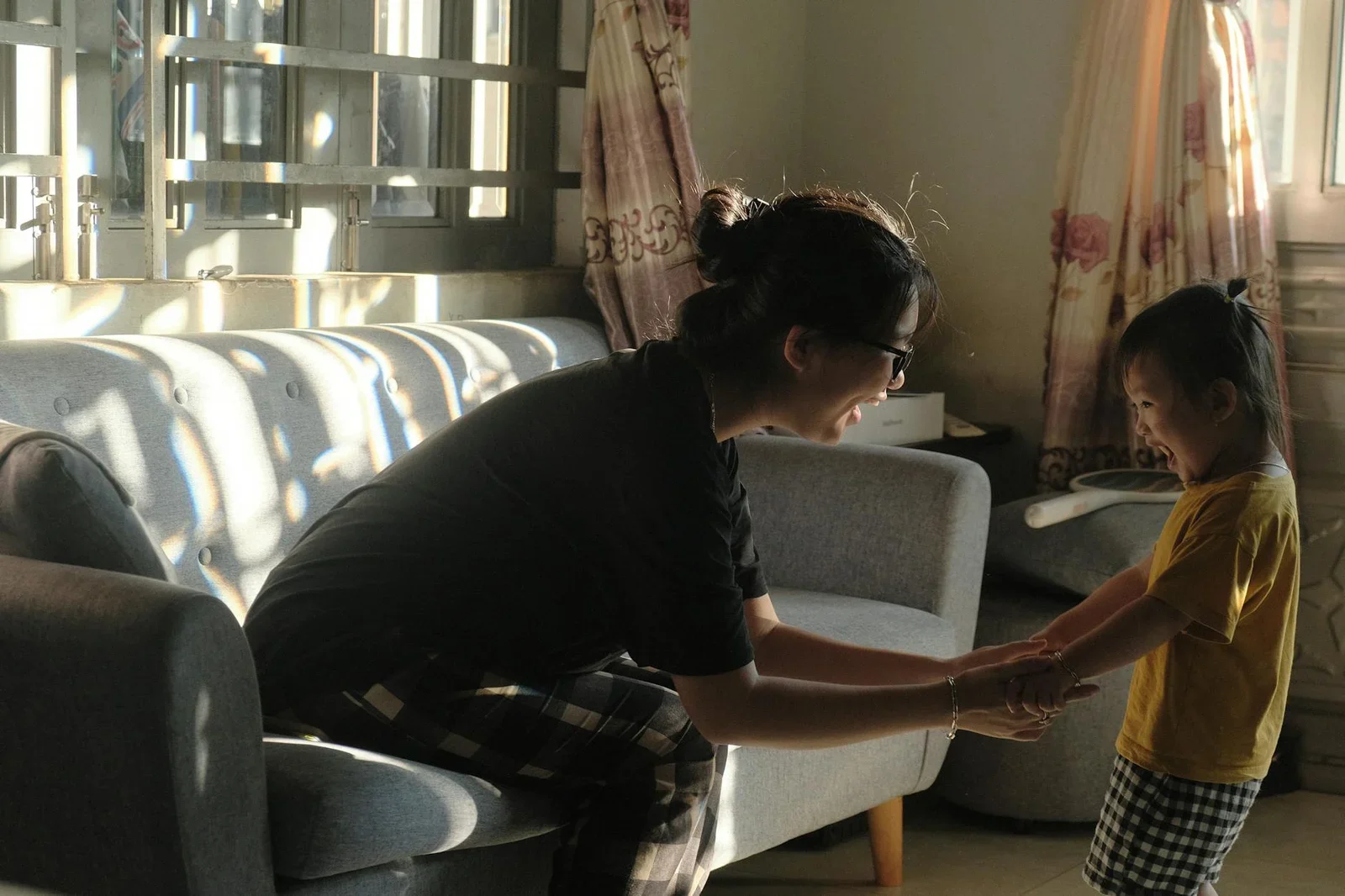 Khoảnh khắc mẹ con nắm tay cười rạng rỡ dưới ánh đèn ấm áp, tôn vinh giá trị sum vầy trong phòng khách mở. | Thiết kế nội thất 24