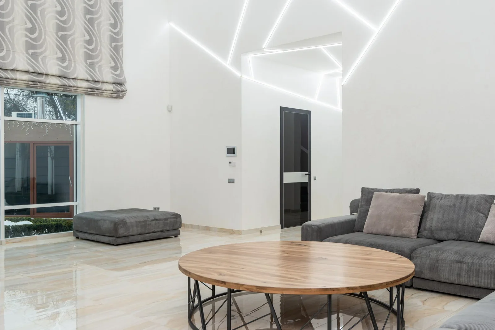 Sofa đặt cạnh bàn gỗ và đôn đệm gần khung cửa rộng, đón ánh sáng tự nhiên giúp phòng khách luôn thông thoáng và gần gũi. | Thiết kế nội thất 24