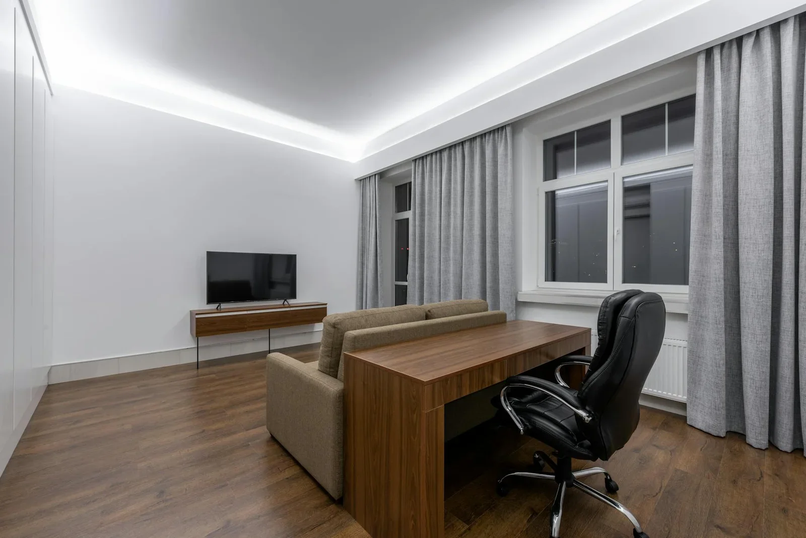 Không gian tối giản rộng rãi với bàn gỗ, sofa và tivi, khéo léo tích hợp góc làm việc vào khu vực tiếp khách. | Thiết kế nội thất 24