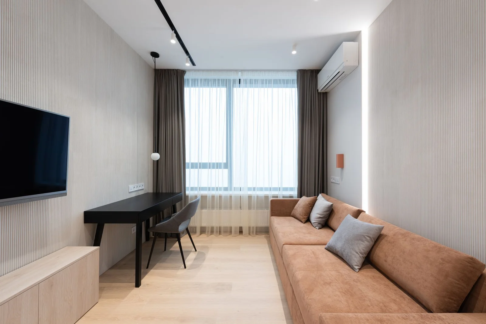 Phòng khách căn hộ hiện đại với ghế sofa có gối ôm hướng tivi treo tường cạnh bàn ghế tạo sự tiện nghi. | Thiết kế nội thất 24