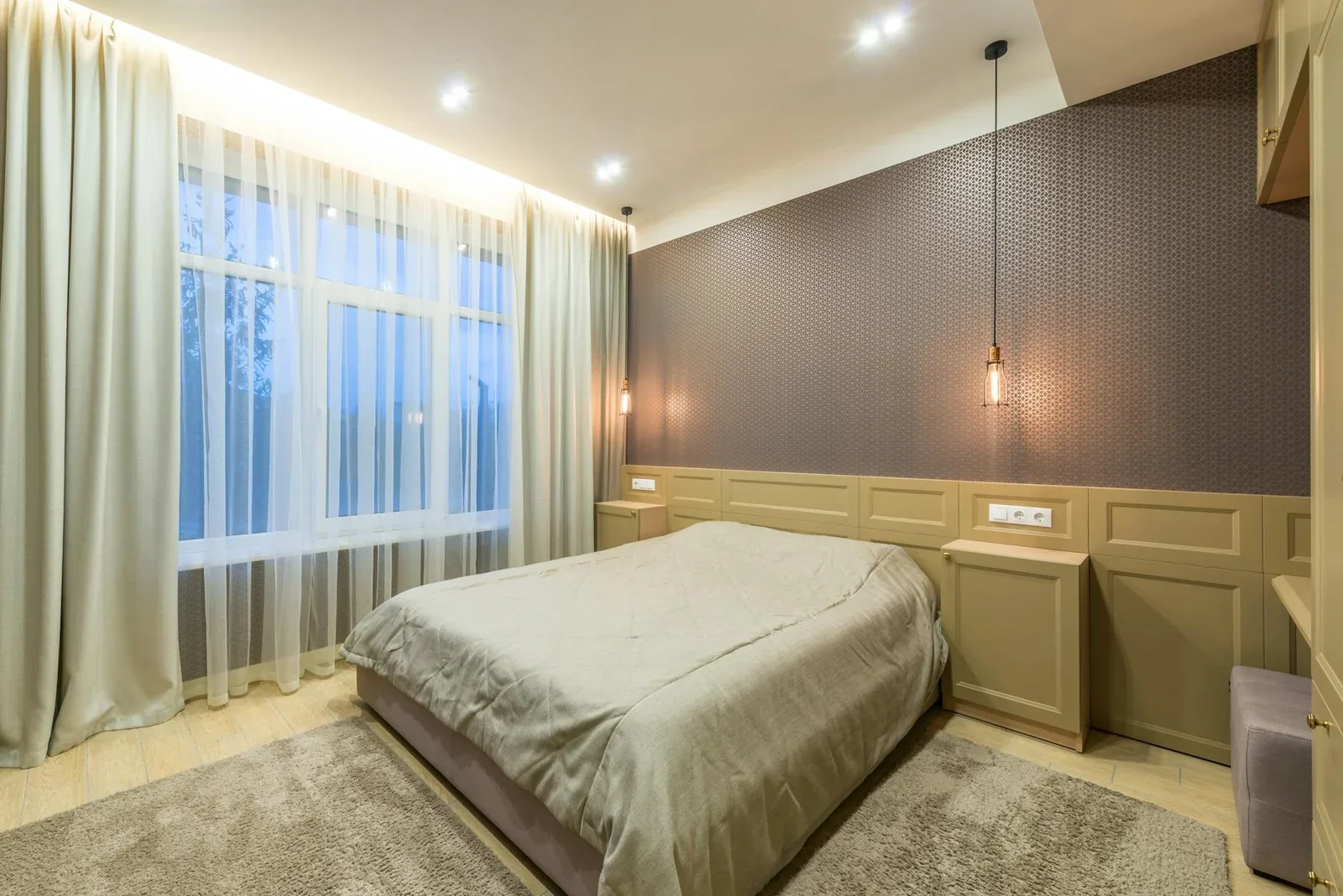 Giường ngủ phủ chăn mềm mại kê sát cửa sổ, nổi bật dưới hệ thống đèn trần căng hiện đại mang lại vẻ đẹp thanh lịch. | Thiết kế nội thất 24