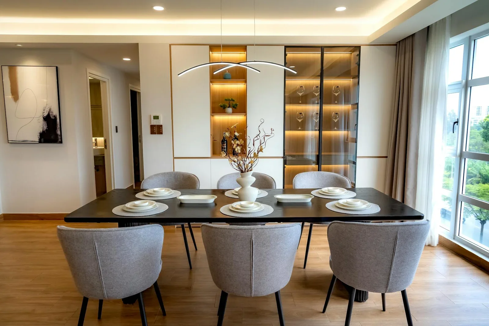 Phòng ăn hiện đại sắp đặt tinh tế cùng đèn thả thanh lịch và tủ kính sang trọng, tạo sự kết nối liền mạch với khu vực bếp. | Thiết kế nội thất 24
