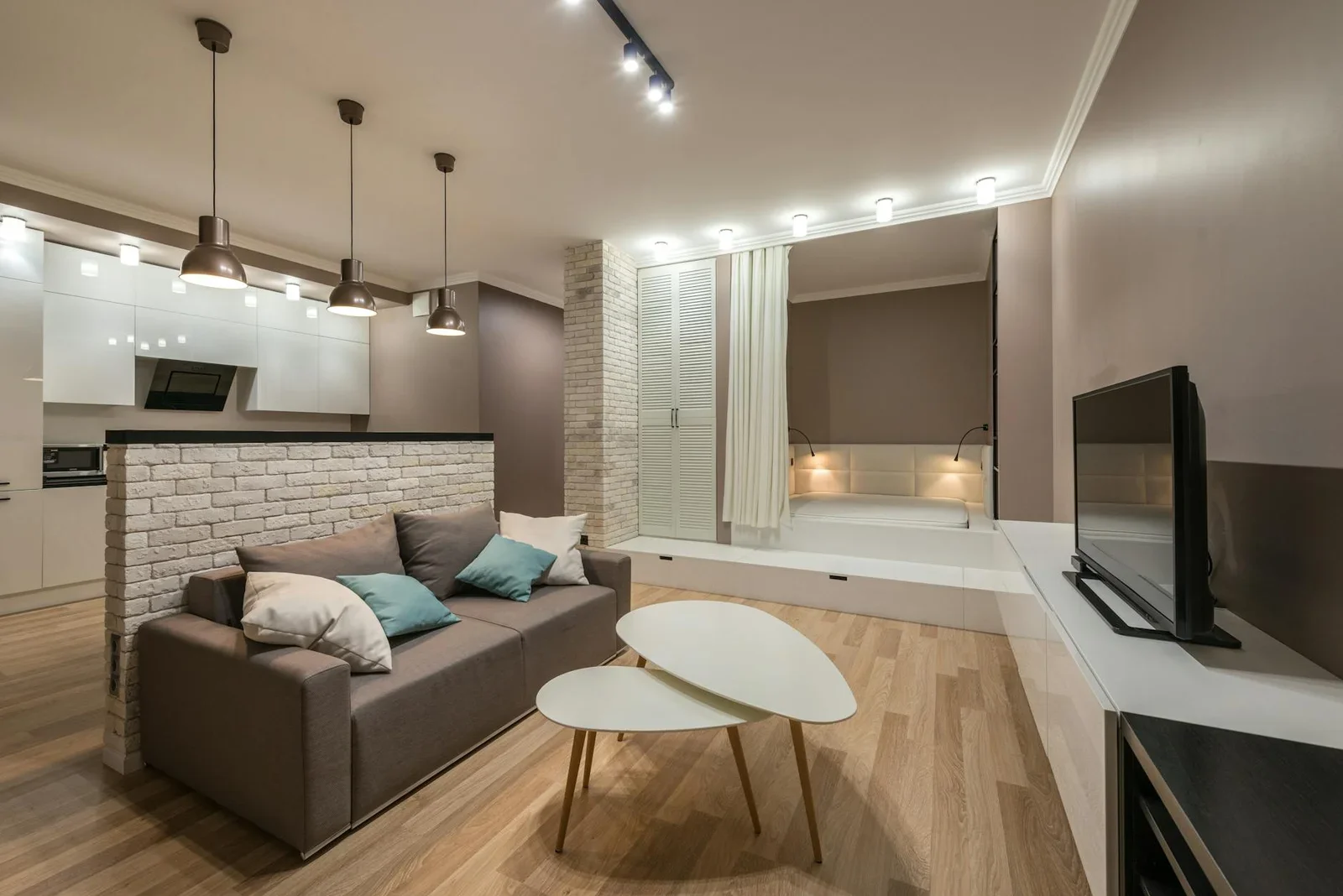 Phòng khách tiện nghi với sofa nhỏ, bàn trà trắng và tivi, tô điểm bằng đèn treo cùng hệ ánh sáng trần dịu nhẹ. | Thiết kế nội thất 24