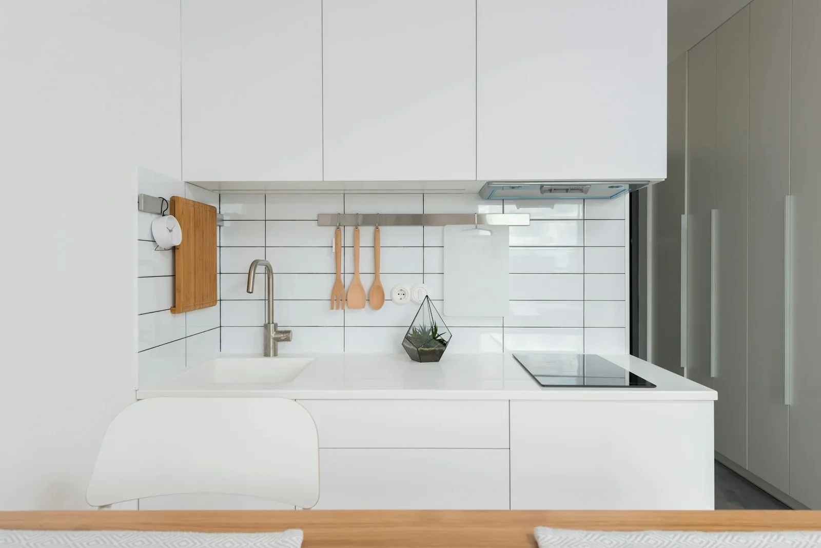 Wooden table placed near white cupboards in modern kitchen w | Thiết kế nội thất 24