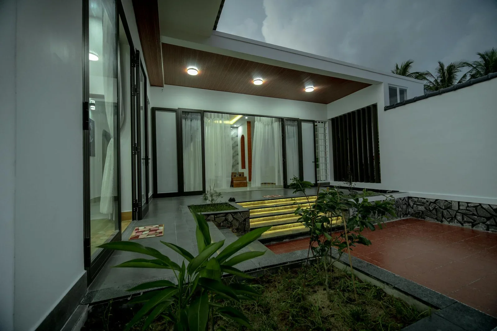 Mặt tiền biệt thự hiện đại nổi bật dưới ánh đèn vàng ấm áp, bao quanh bởi thảm cây xanh mát giữa đêm tĩnh lặng. | Thiết kế nội thất 24