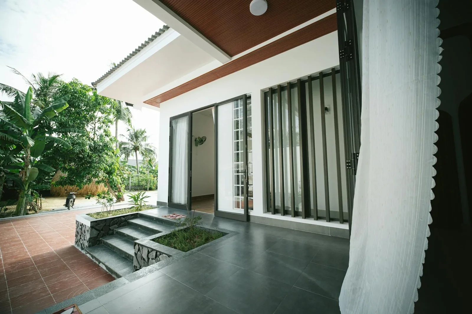 Sân vườn rộng rãi kết nối hài hòa với hiên nhà thoáng đãng, tận dụng ánh sáng ban ngày tôn lên vẻ đẹp xanh mát. | Thiết kế nội thất 24