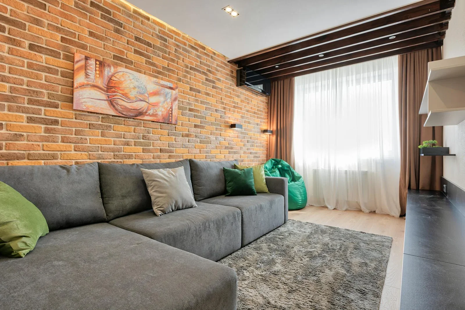 Không gian tiếp khách nổi bật với sofa xám rộng, tường gạch thô mộc và ánh nắng xuyên qua rèm voal tạo nét phóng khoáng. | Thiết kế nội thất 24