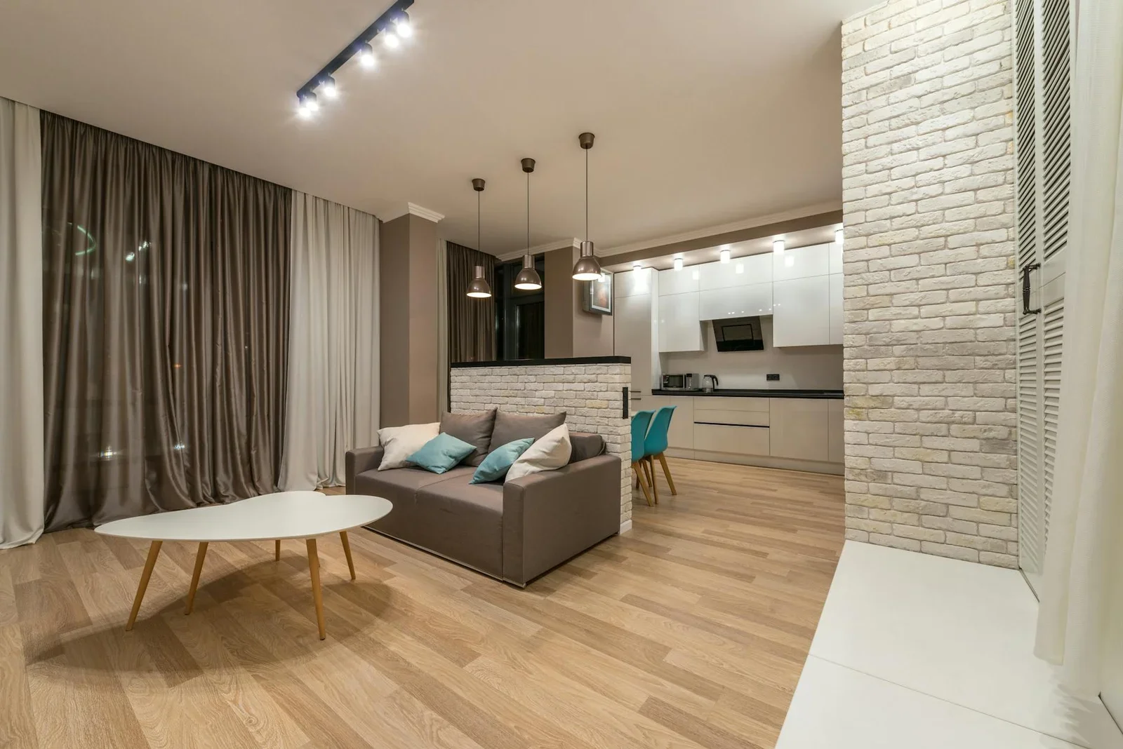Ghế sofa êm ái kê gần bàn trà, kết nối liền mạch với khu bếp hiện đại qua khung cửa rèm che mềm mại. | Thiết kế nội thất 24