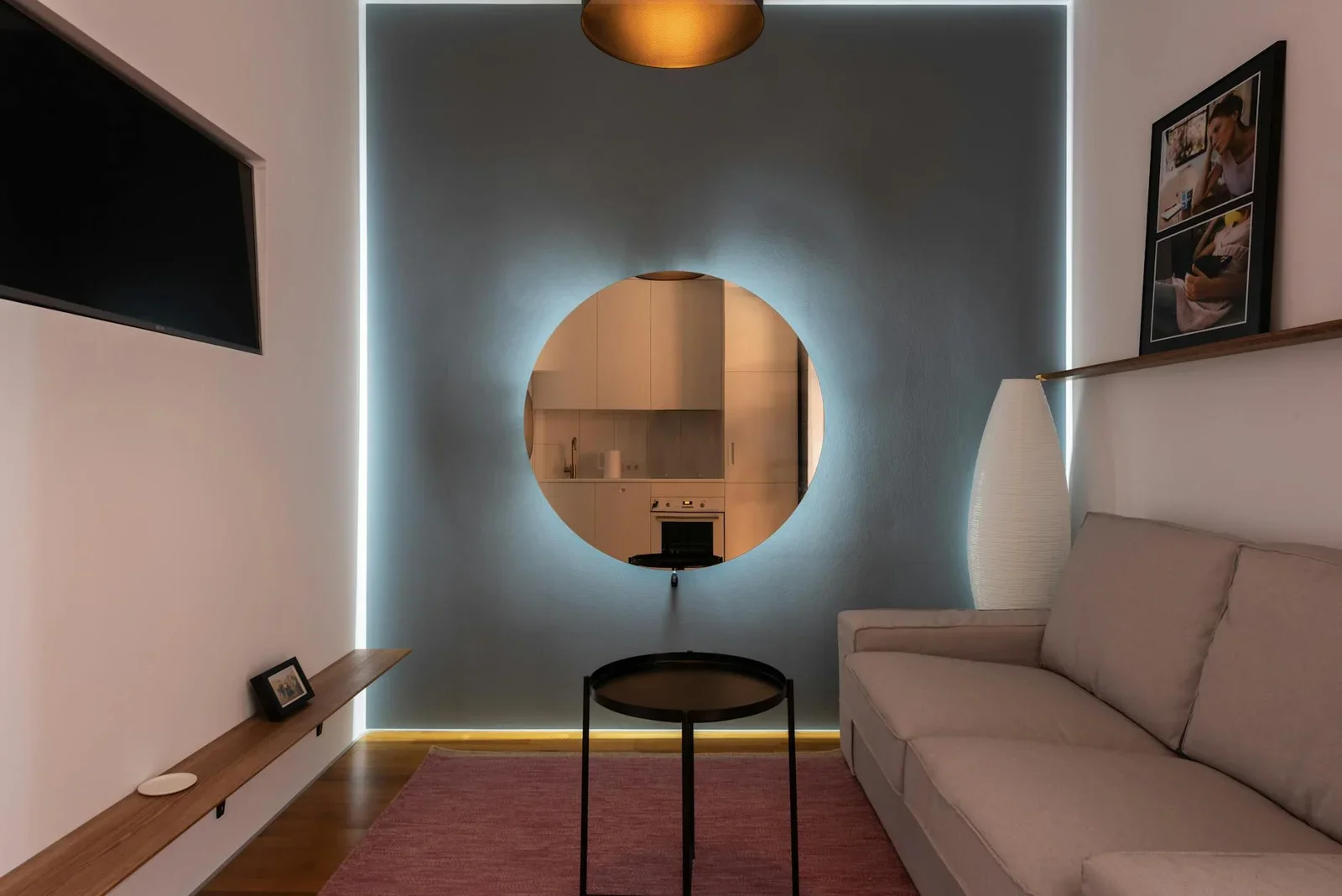 Khu giải trí hiện đại với khung tranh, sofa êm ái đối diện tivi, tường sáng kết hợp gương tròn tạo hiệu ứng rộng rãi. | Thiết kế nội thất 24