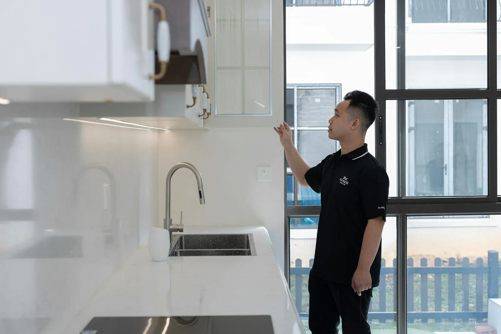 Kiến trúc sư kiểm tra chi tiết tủ bếp trong căn hộ hiện đại sở hữu khung cửa kính rộng đón sáng tự nhiên. | Thiết kế nội thất 24
