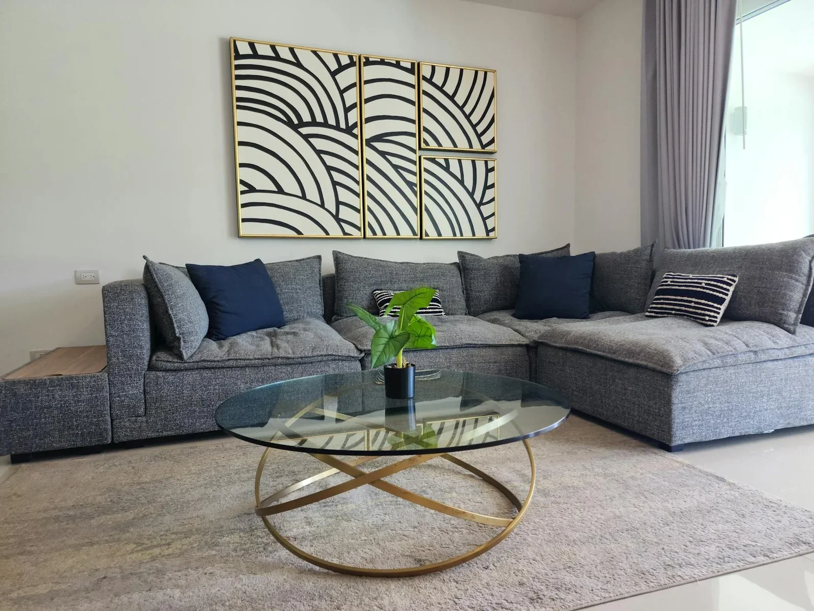 Phòng khách hiện đại với sofa góc xám, bàn trà kính và tranh trừu tượng, kiến tạo không gian sinh hoạt lý tưởng cho nhà cấp bốn. | Thiết kế nội thất 24