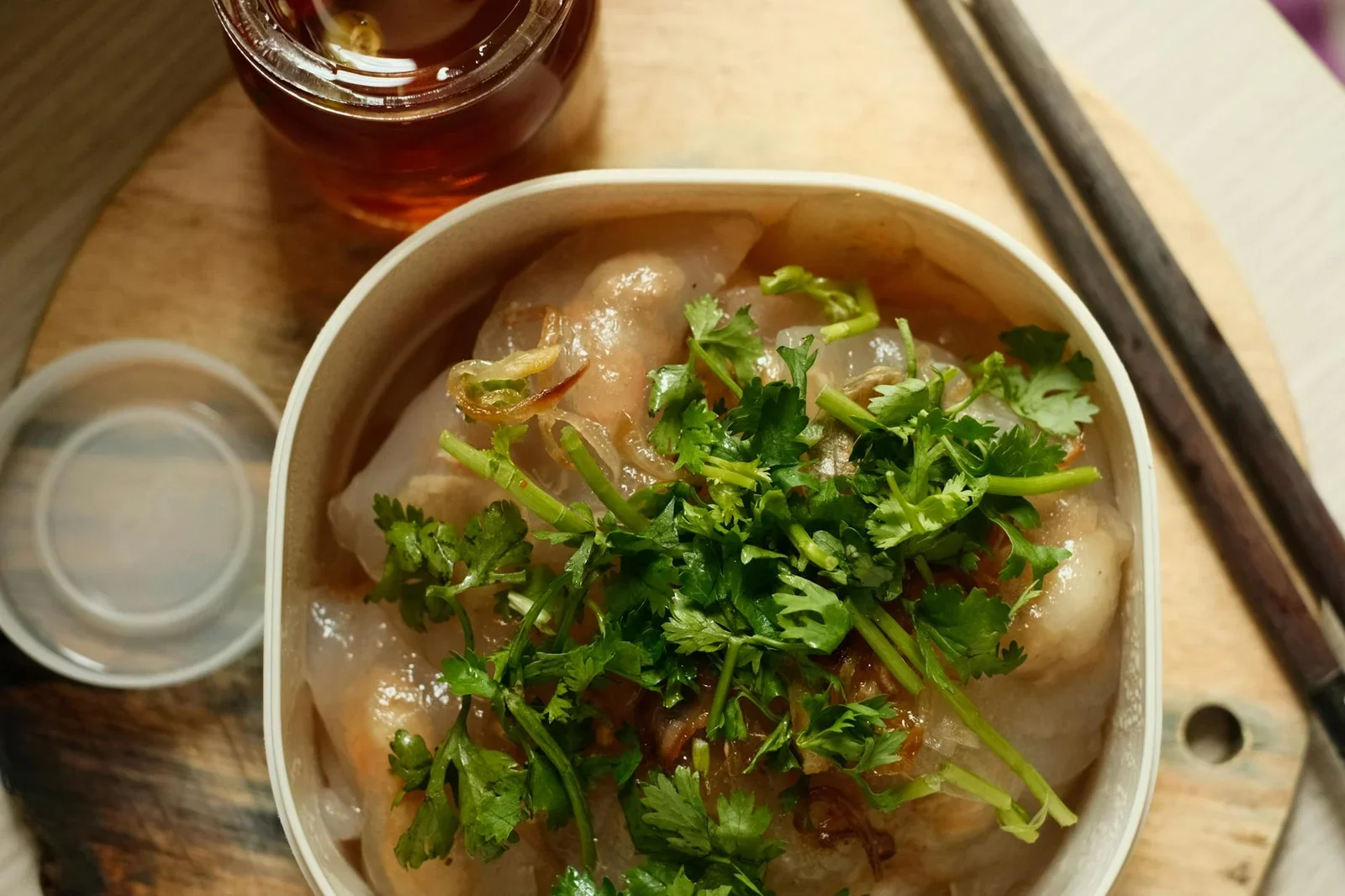 Bánh hấp mềm mịn điểm rau thơm cạnh tách trà và đũa gỗ, tạo bố cục tĩnh vật cân đối dưới ánh sáng dịu. | Thiết kế nội thất 24