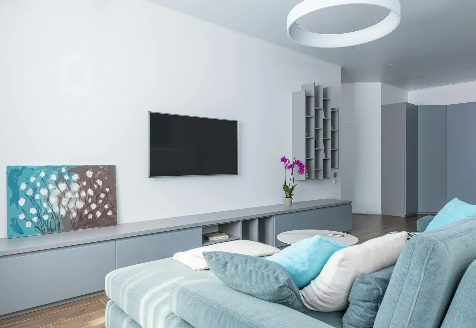Phòng khách rộng rãi phong cách hiện đại với kệ xám tinh tế, điểm xuyết chậu hoa tím cùng tranh treo tường tạo sức sống mới. | Thiết kế nội thất 24
