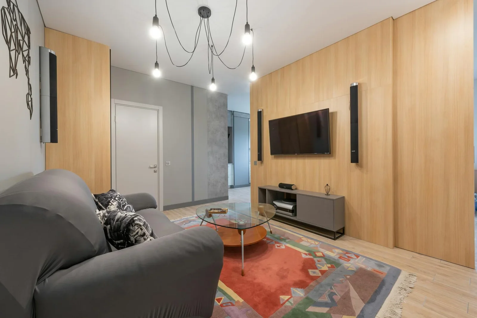 Phòng khách hiện đại với sofa êm ái, bàn kính trên thảm trải sàn và hệ tủ tivi, đèn trần tạo điểm nhấn sang trọng. | Thiết kế nội thất 24