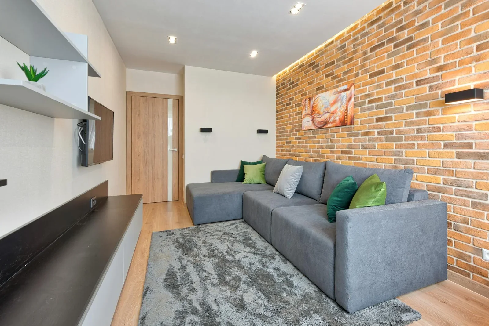 Phòng khách hiện đại nổi bật với sofa chữ L màu xám, tường gạch thô cùng đồ trang trí tinh tế, mang lại vẻ đẹp thời thượng. | Thiết kế nội thất 24