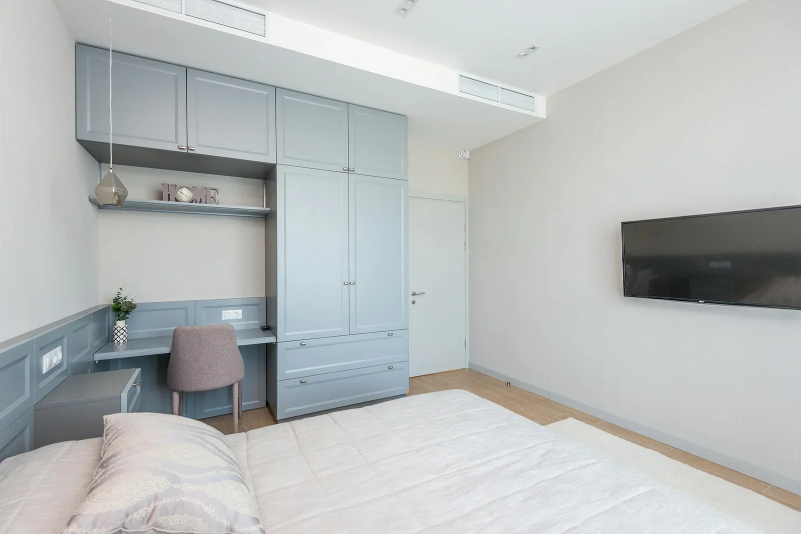 Phòng ngủ duplex tối giản nổi bật với tủ áo xanh dương, tivi treo tường gọn gàng và ánh sáng tự nhiên tươi mới. | Thiết kế nội thất 24