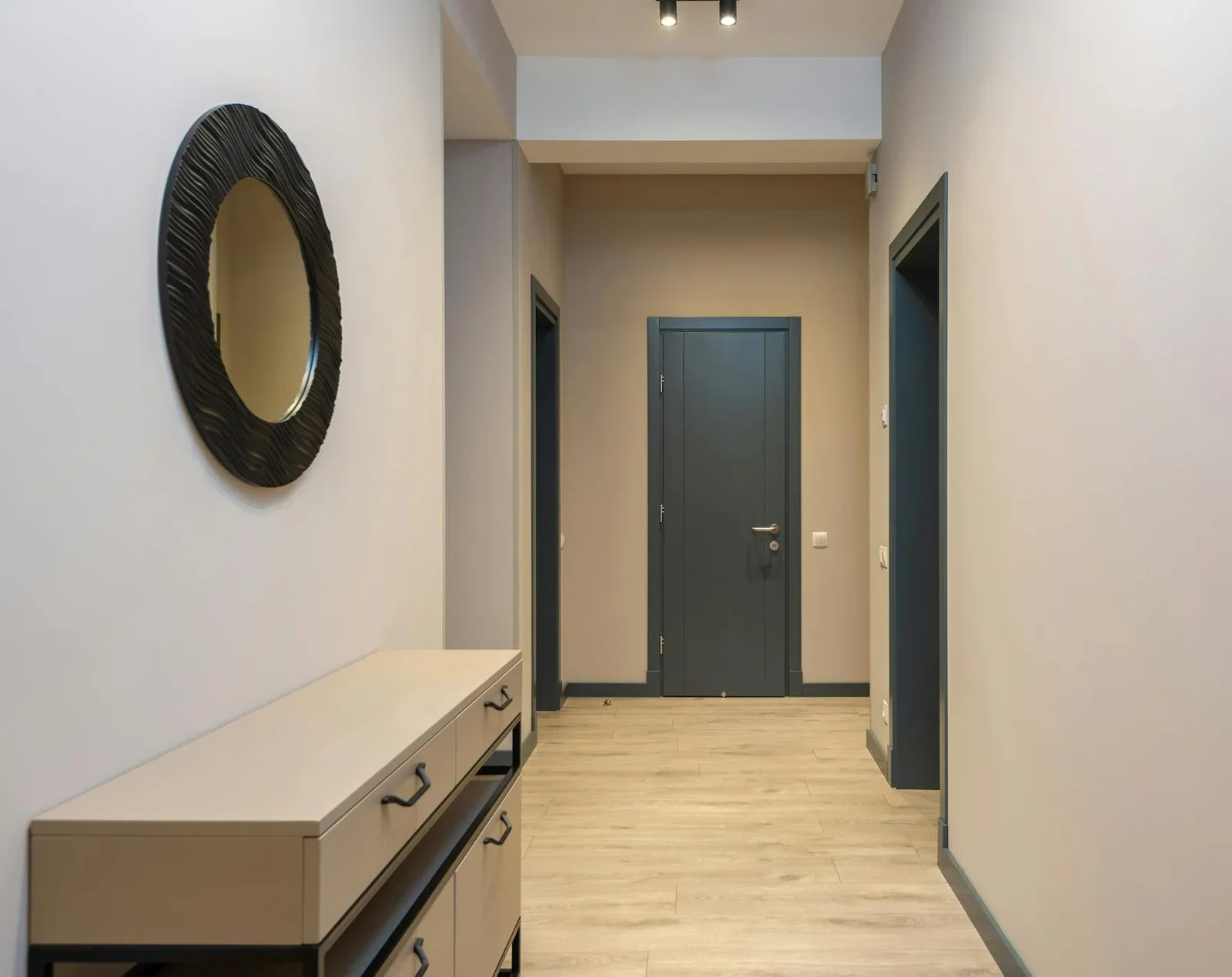 Gương tròn nghệ thuật treo trên tủ gỗ hành lang, kết hợp sàn gỗ ấm áp và tường beige, tạo điểm nhấn thanh lịch cho lối đi. | Thiết kế nội thất 24