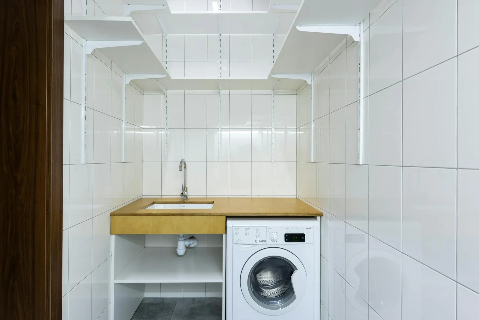 Góc giặt giũ hiện đại lát gạch trắng sạch sẽ, bố trí máy giặt cùng kệ âm tường gọn gàng, nâng cao tiện ích sinh hoạt. | Thiết kế nội thất 24