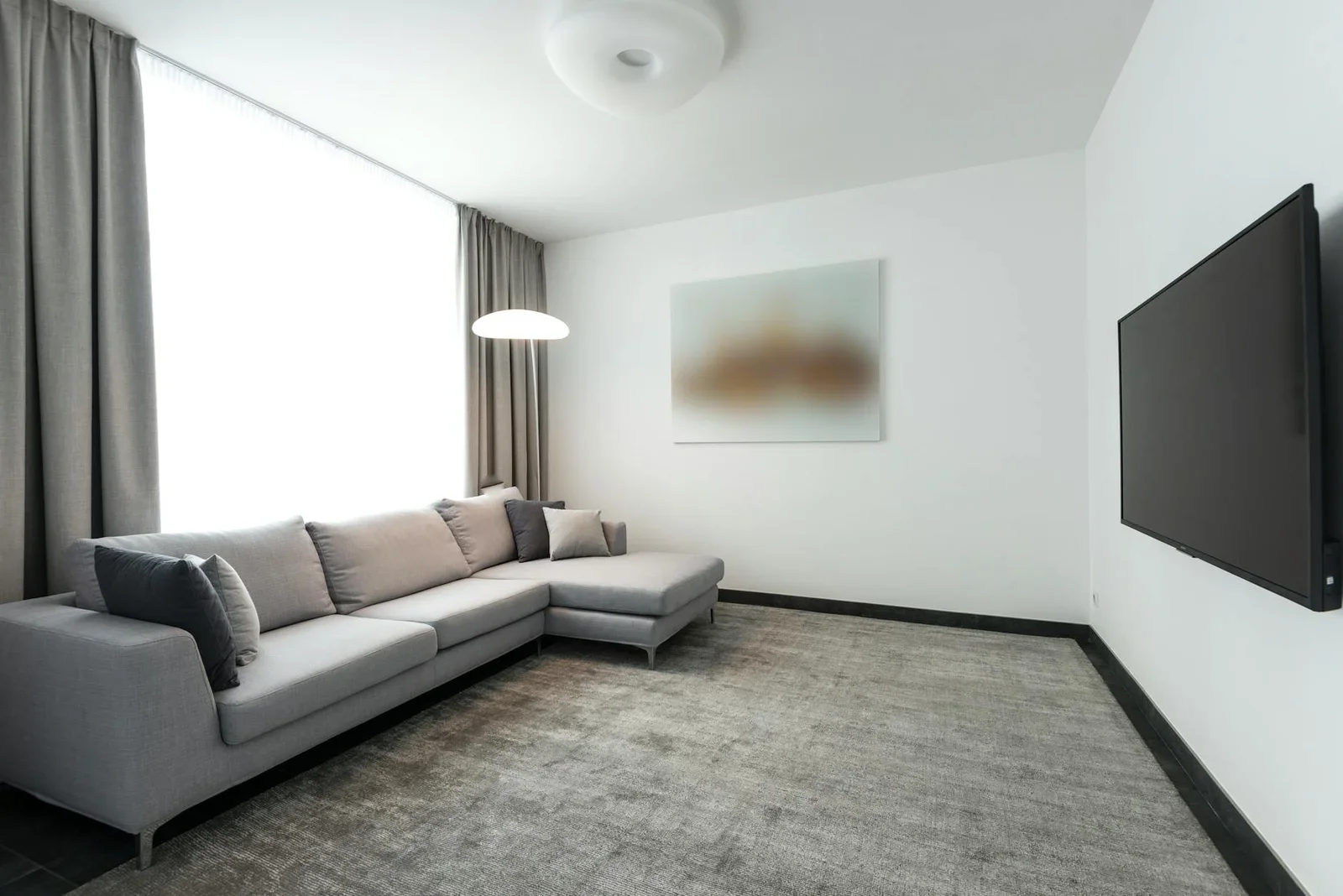 Phòng khách hiện đại rộng rãi với sofa chữ L màu xám và tivi màn hình phẳng, mang đậm nét tối giản tinh tế. | Thiết kế nội thất 24