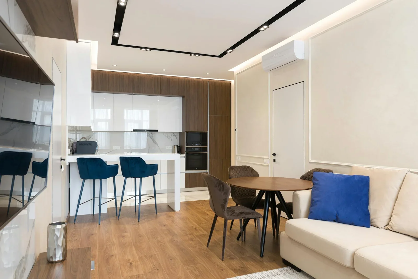 Sofa êm ái cùng đệm mềm đặt trước tivi trong căn hộ studio hiện đại, tích hợp liền mạch khu bếp và bàn ăn gọn gàng. | Thiết kế nội thất 24
