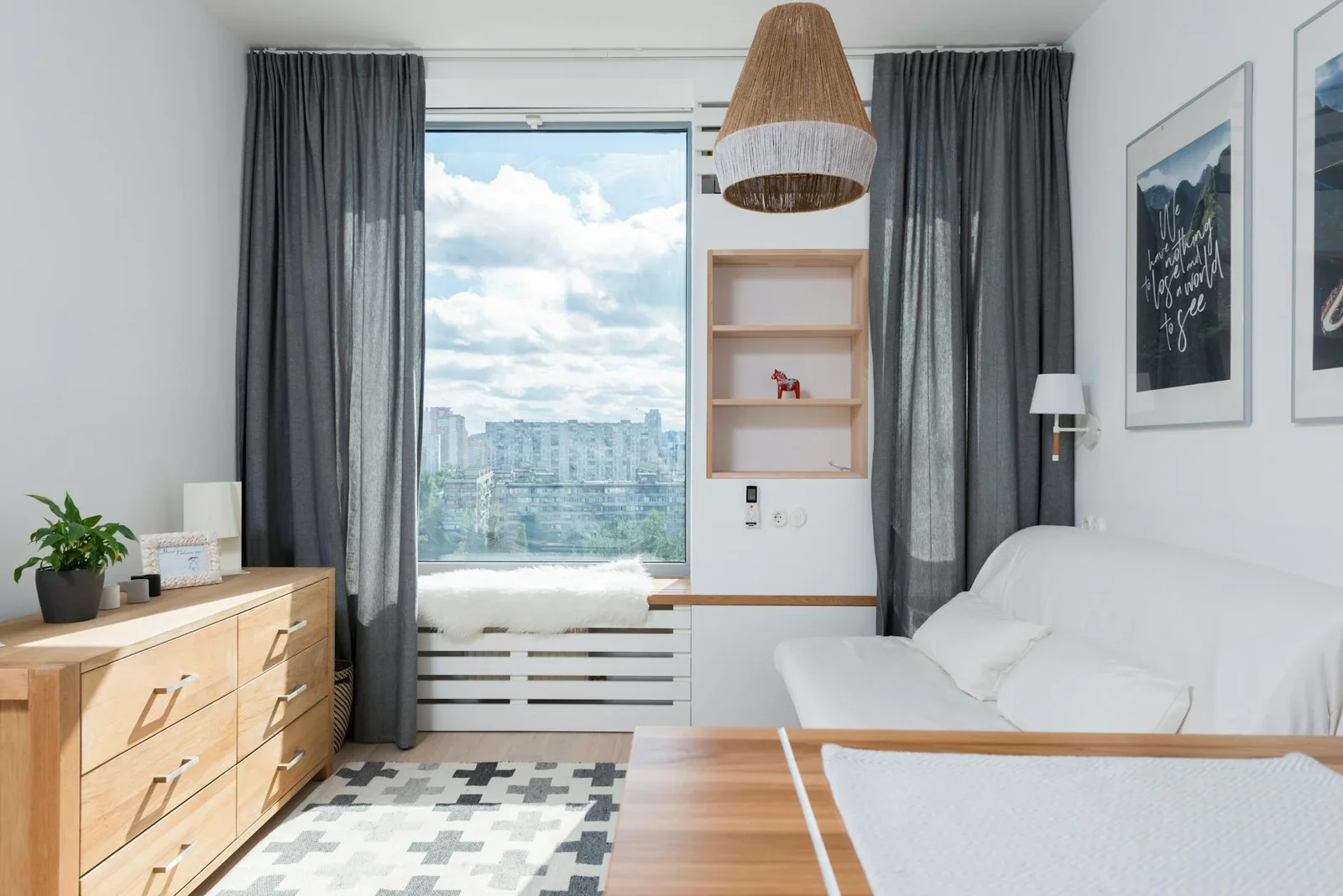 Bàn gỗ và tủ thấp kề sofa trắng tựa tường treo tranh nghệ thuật, đón nắng tự nhiên tạo không gian thời thượng đầy sinh khí. | Thiết kế nội thất 24