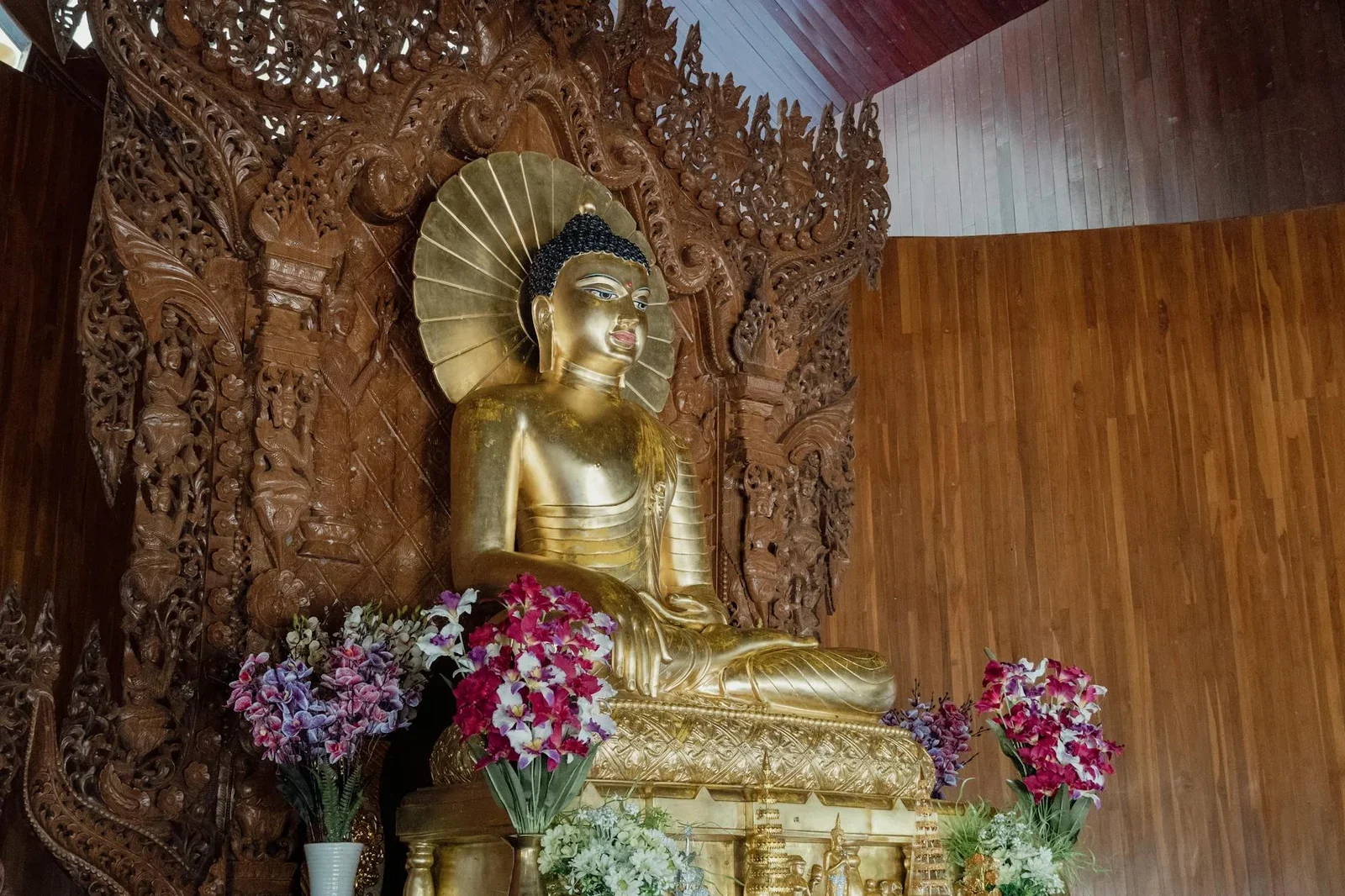 Tượng Phật mạ vàng trong khám gỗ chạm khắc tỉ mỉ, hoa tươi điểm xuyết cùng ánh sáng dịu nhẹ tôn nét trang nghiêm. | Thiết kế nội thất 24