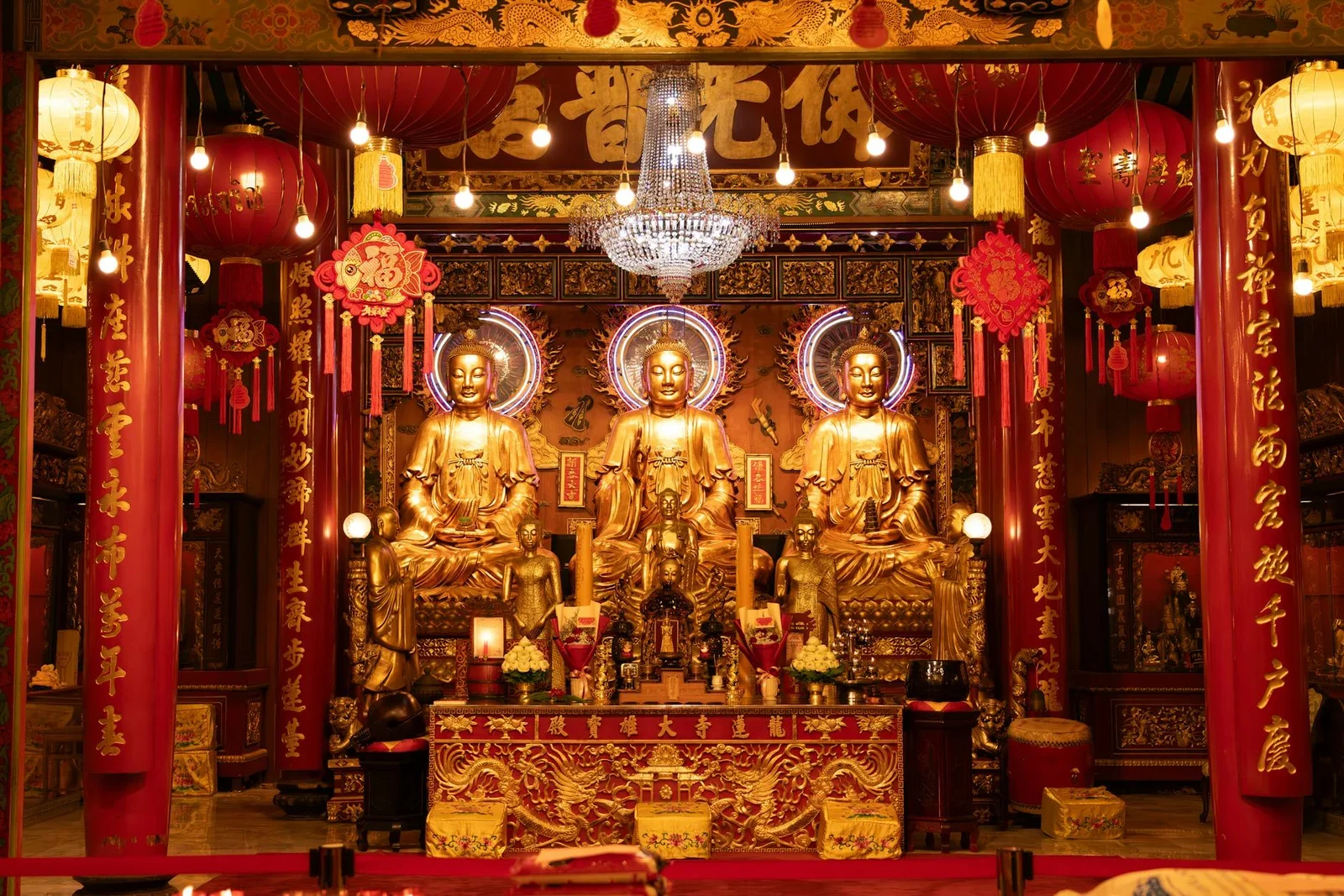 Ba tượng Phật mạ vàng uy nghi giữa điện thờ, cột đỏ sơn mài cùng đèn lồng tỏa sáng ấm áp tạo không gian thiền tịnh. | Thiết kế nội thất 24